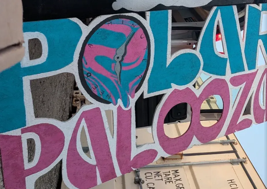Hand-painted Polar Palooza sign in aqua and pink, with the melting Need a Minute pocket watch painted inside the O